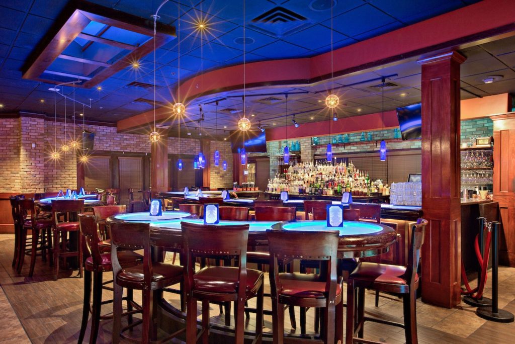 Restaurant with wooden furniture, neon lights and a curved bar at Sage Woodfire Tavern