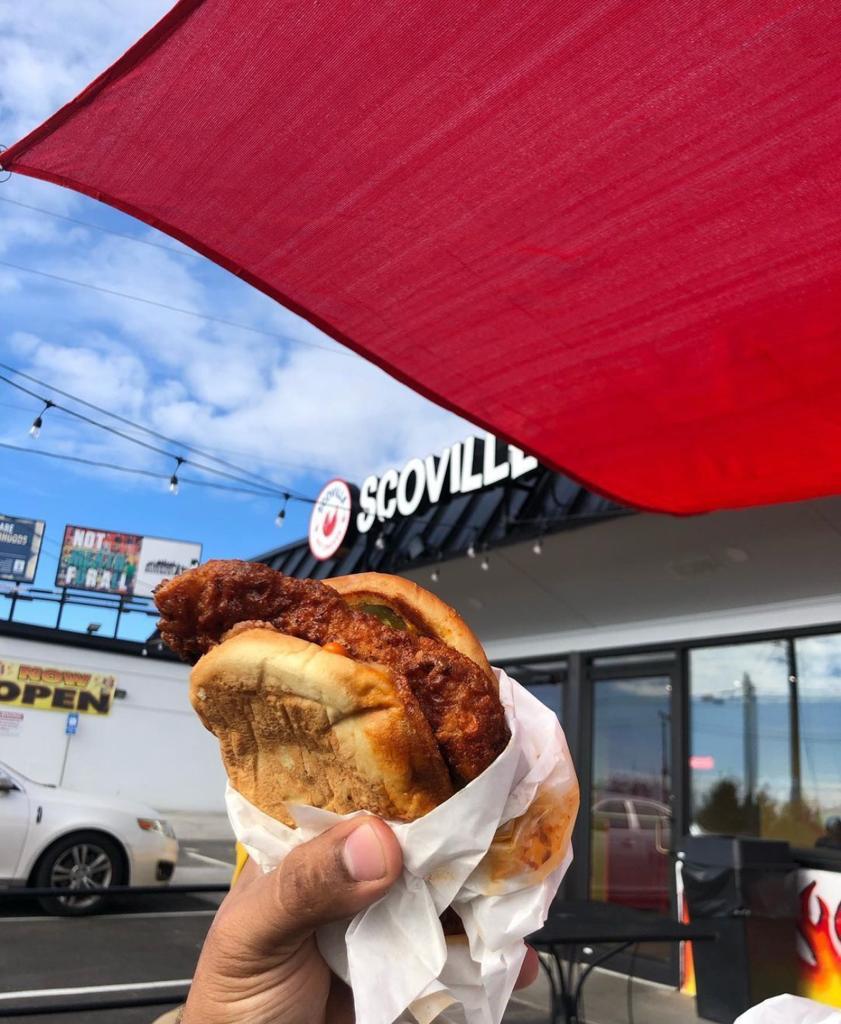 Hand holding up chicken sandwich outside building of Scoville Hot Chicken in Midtown