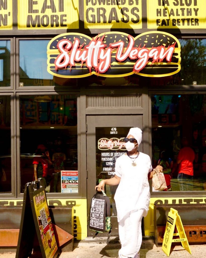 Customer in white clothing posing front of the Slutty Vegan sign and entrance
