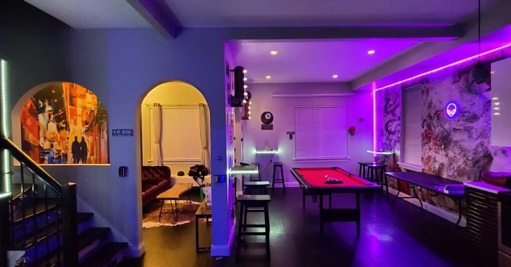 Neon lighted gaming room with a billiard table, stools and art covered walls at Coexist Gaming Arcade and Lounge