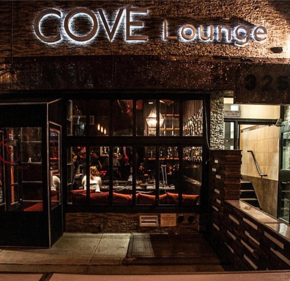 Restaurant with brick façade, floor to ceiling windows and the Cove Lounge sign lighted above a black entrance booth at Cove Lounge