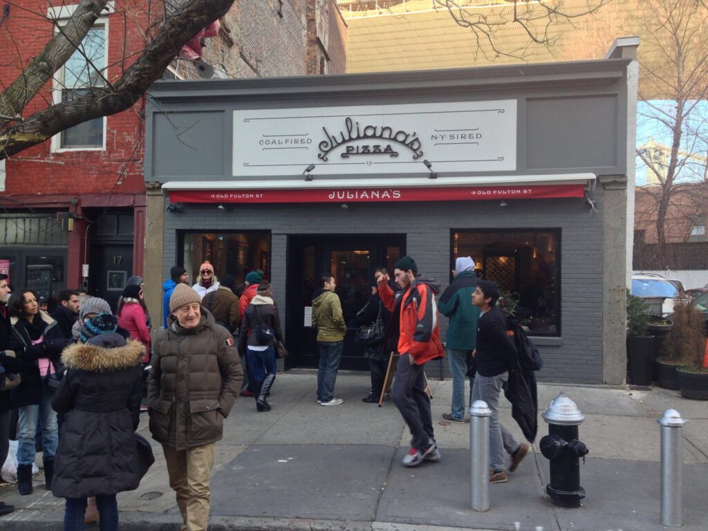 Passersby walking past gray building with the Juliana's Pizza signage above a folded up awning