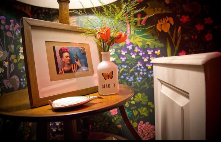 Framed picture of Frida Kahlo set on a stool placed against a wall full of floral paintings at Kahlo