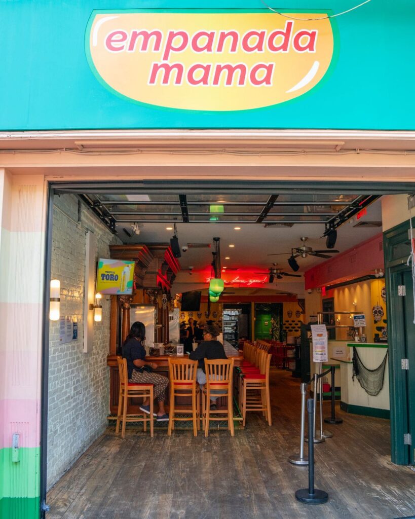 Restaurant exterior with teal walls holding a floor to ceiling window at Empanada Mama