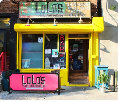 Yellow storefront with window display with pink sign, and cracked pavement at Lolo's Seafood Shack