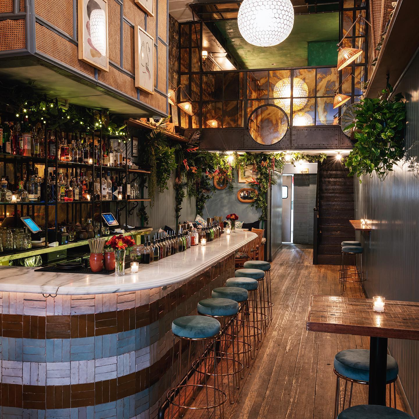Earth toned bar with wooden floors, gray walls and stools, big round chandelier and plants on the walls at Las' Lap