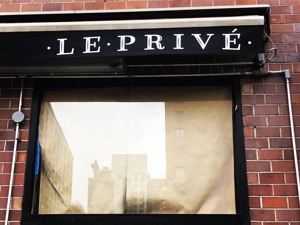 Store front with glass window below a black awning bearing the Le Prive Name