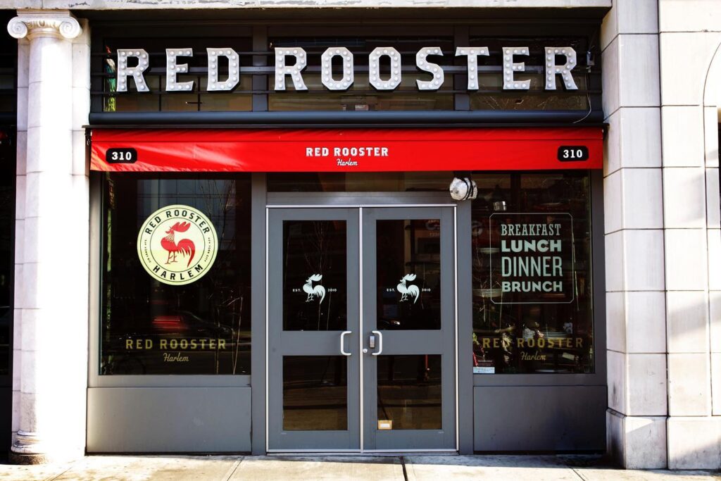 Outside view of restaurant with the Red Rooster name above a glass doors and windows at Red Rooster