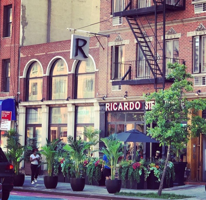 Restaurant exterior with black paneling bearing Ricardo in red letters and decorated with potted palms at Ricard Steak House