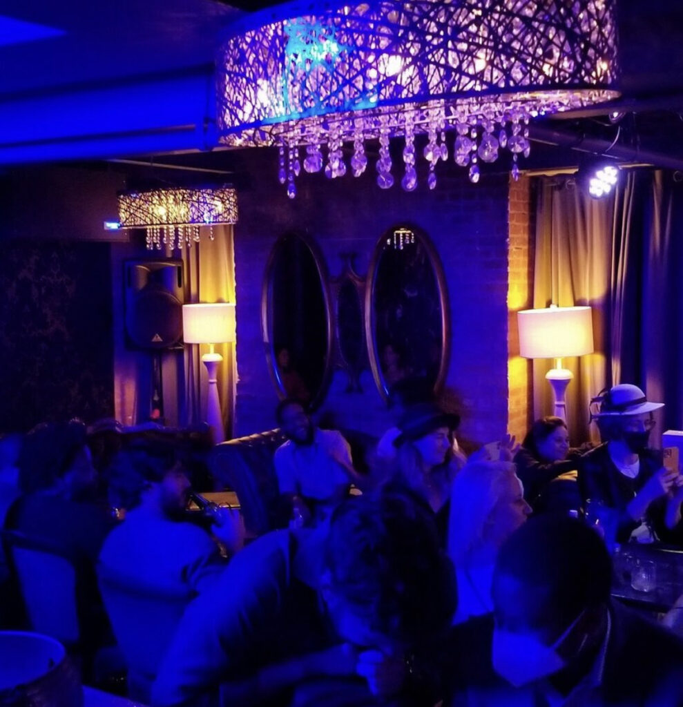 Patrons seated at a bar awash with blue lights with a chandelier overhead at Room 623