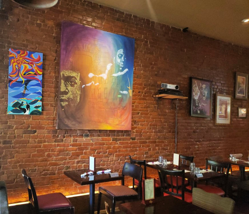 Restaurant with dark, wooden furniture and art covered brick wall covered in colorful art at Rustik Tavern