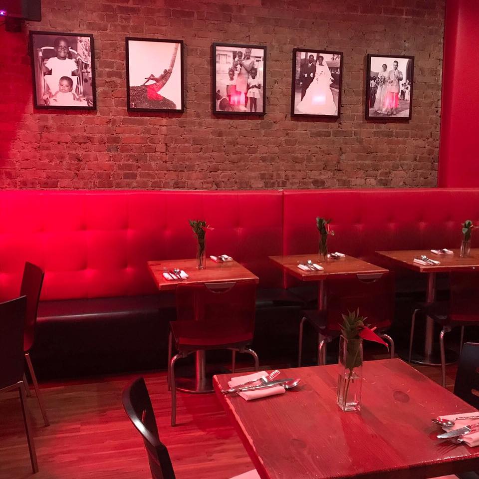 Eating area colored with red lights and furnished with a long, red sofa placed against a brick wall at Sugarcane.