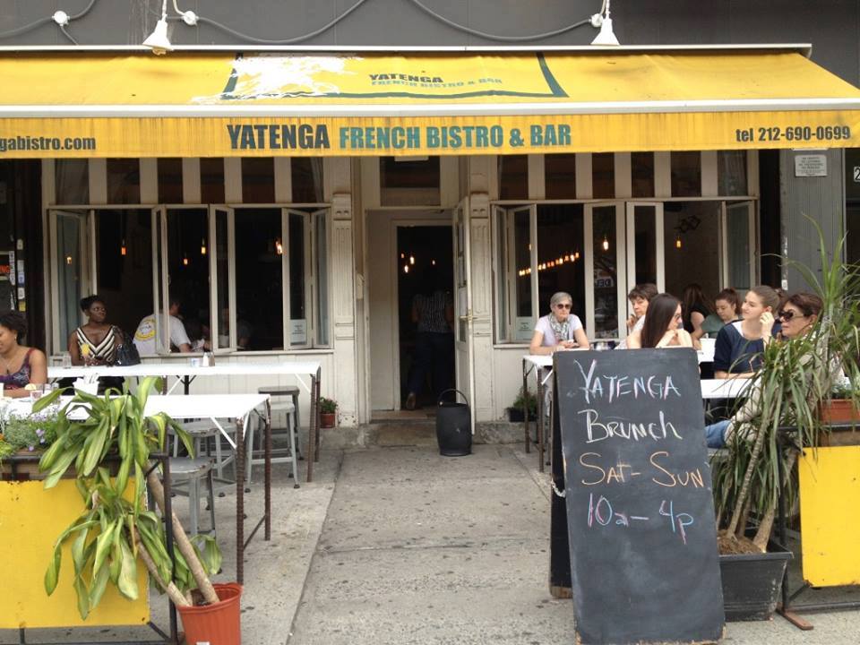 Outdoor dining at Yatenga French Bistro and Bar; patrons seated at white tables under the shade of a yellow awning.