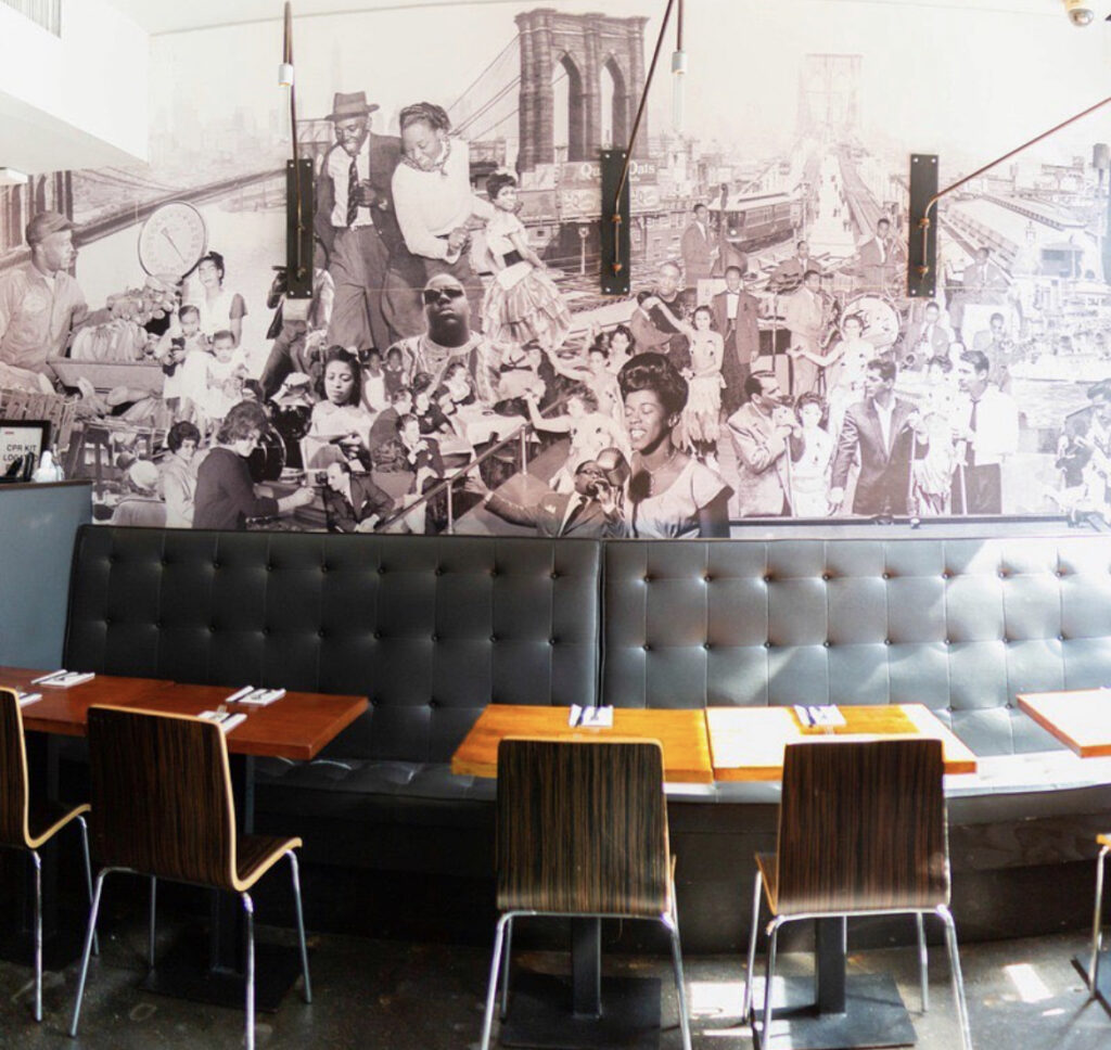 Wooden tables, chairs and a black sofa set against a mural covered wall at SoCo