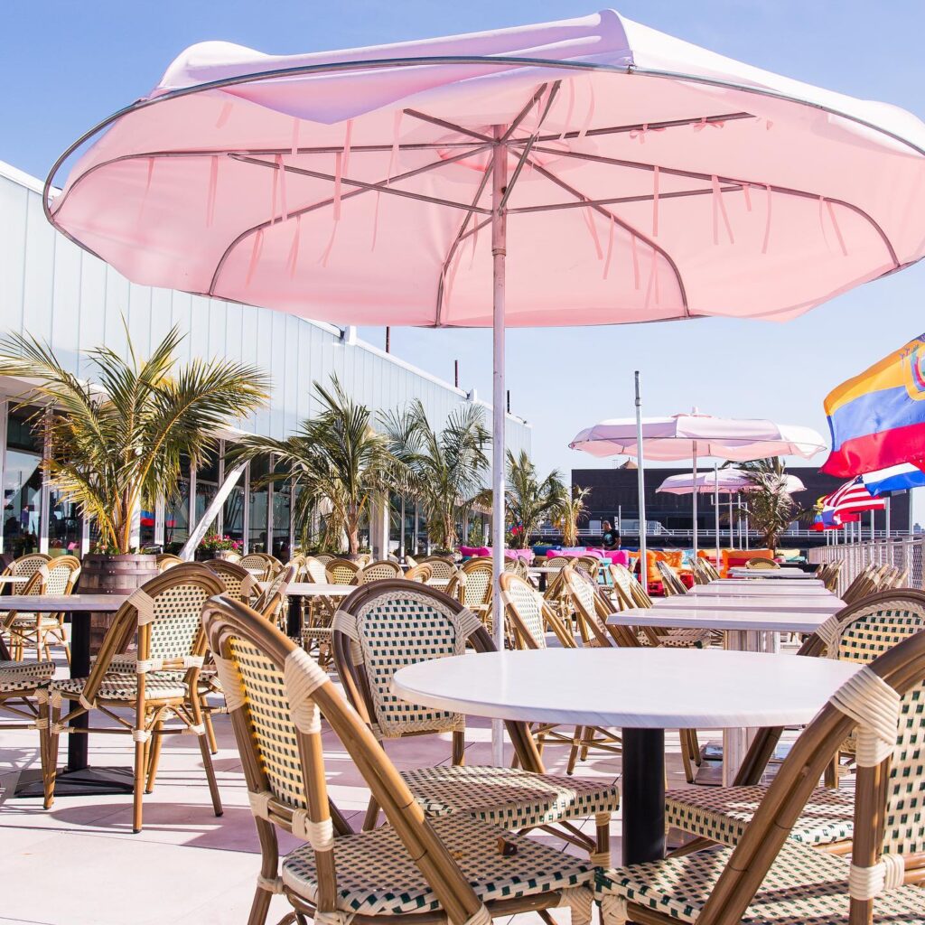 Pink umbrellas, white tables, potted palms at the rooftop of Zona de Cuba